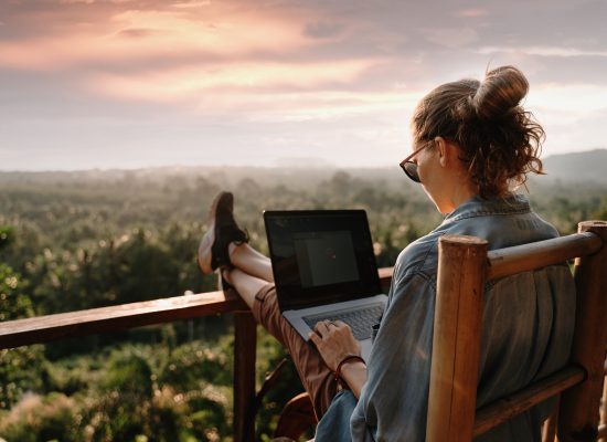 Young business woman working at the computer in cafe on the rock. Young girl downshifter working at a laptop at sunset or sunrise on the top of the mountain to the sea, working day.